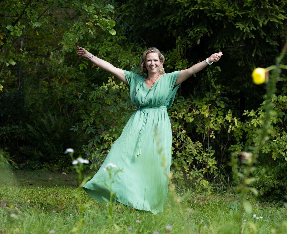 Martina Klein (5) Martina KLein mit einem langen Kleid und ausgebreiteten Armen auf einer Blumenwiese